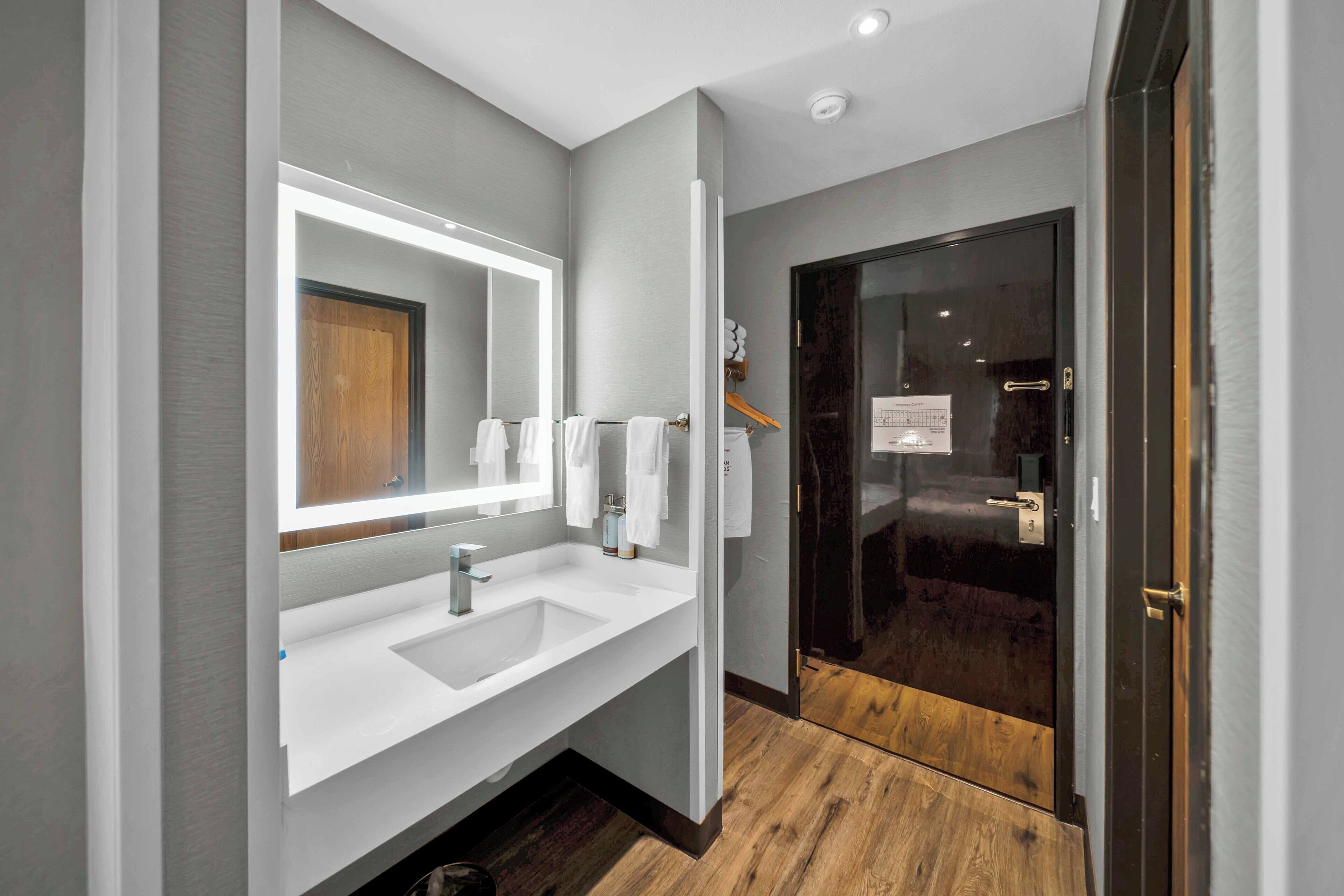 A modern bathroom with a large mirror, white sink, and dark wooden door.