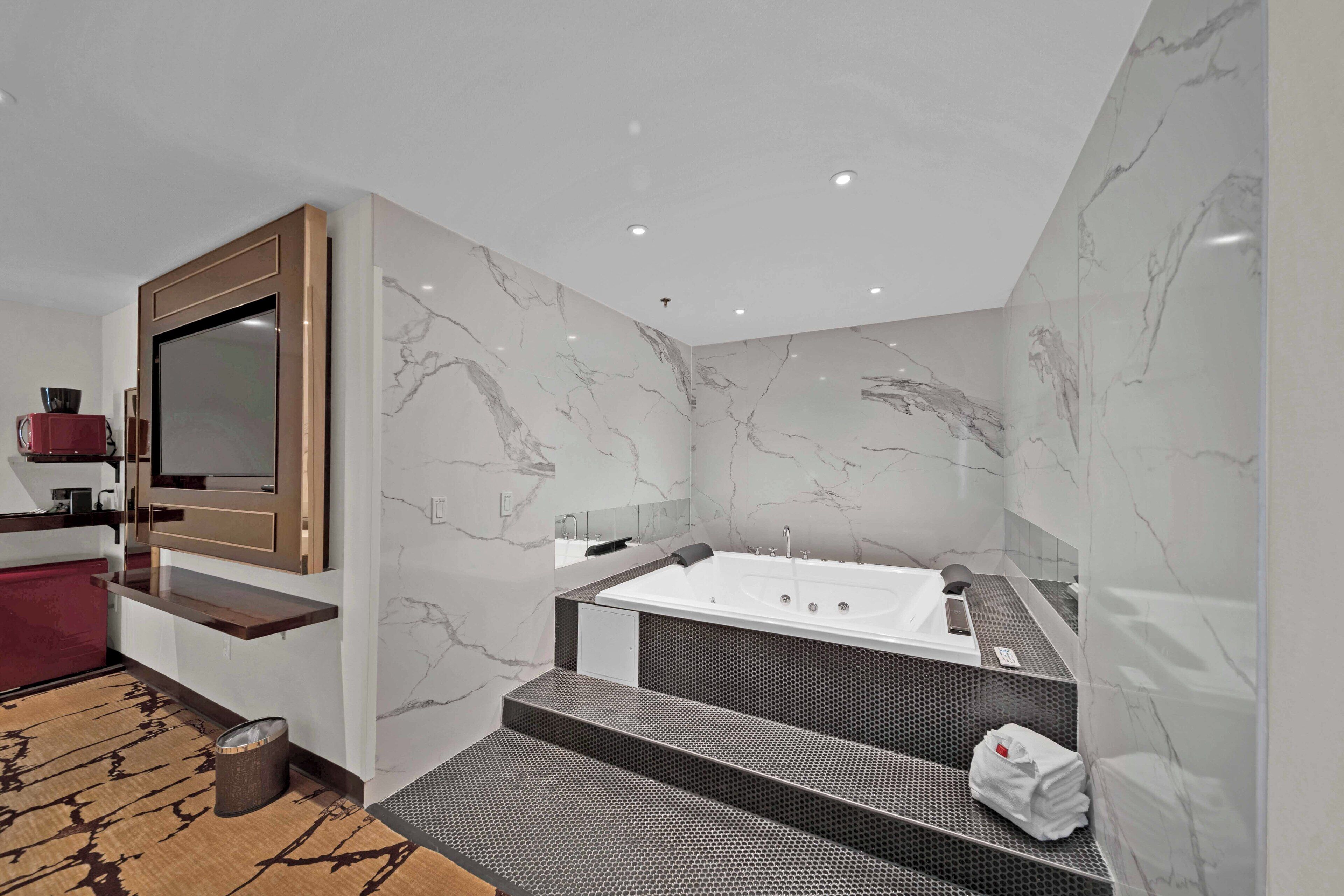 Een moderne badkamer met een marmeren wand, een groot ligbad en een houten wastafelmeubel.