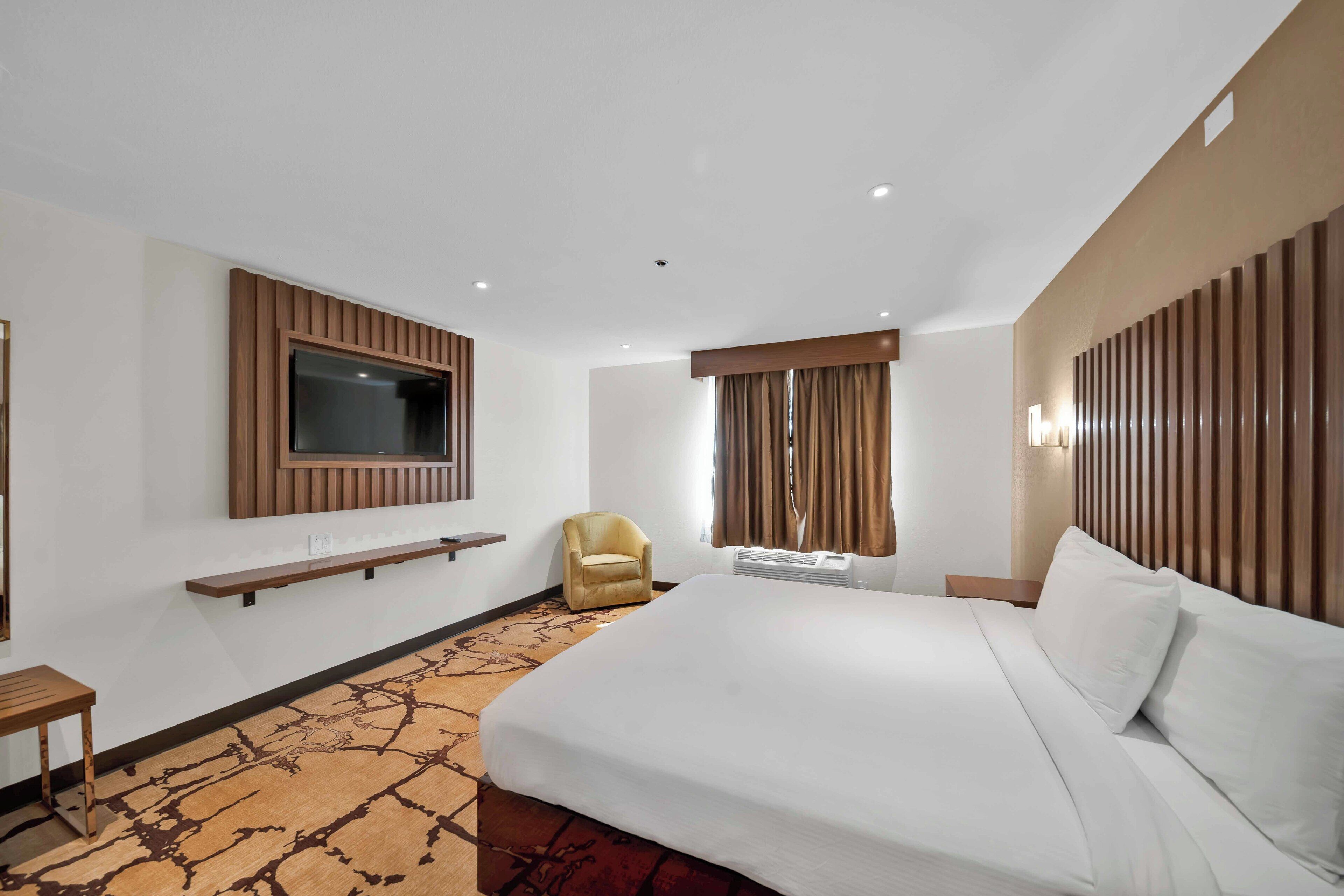 Een hotelkamer met een groot bed, een aan de muur bevestigde televisie, een stoel en een bureau.