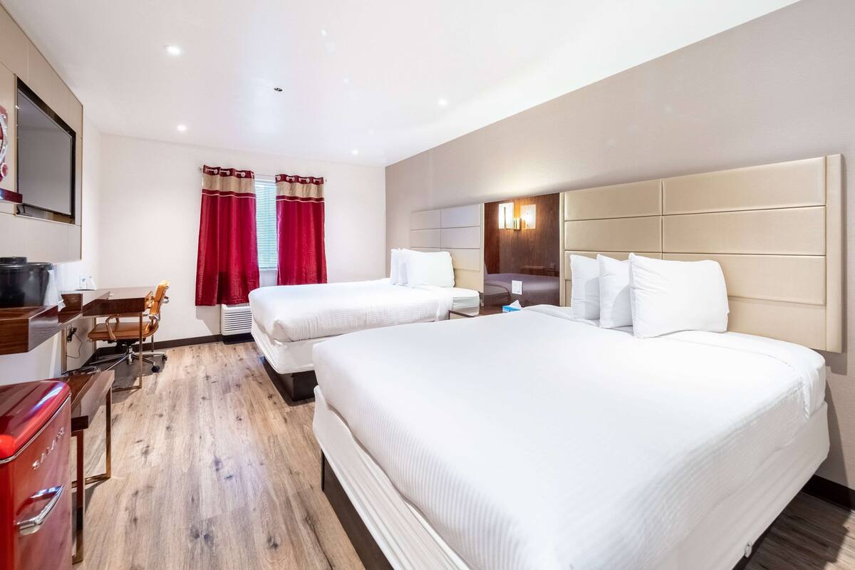 A hotel room with two beds, a desk with a chair, a TV, and a red curtain.