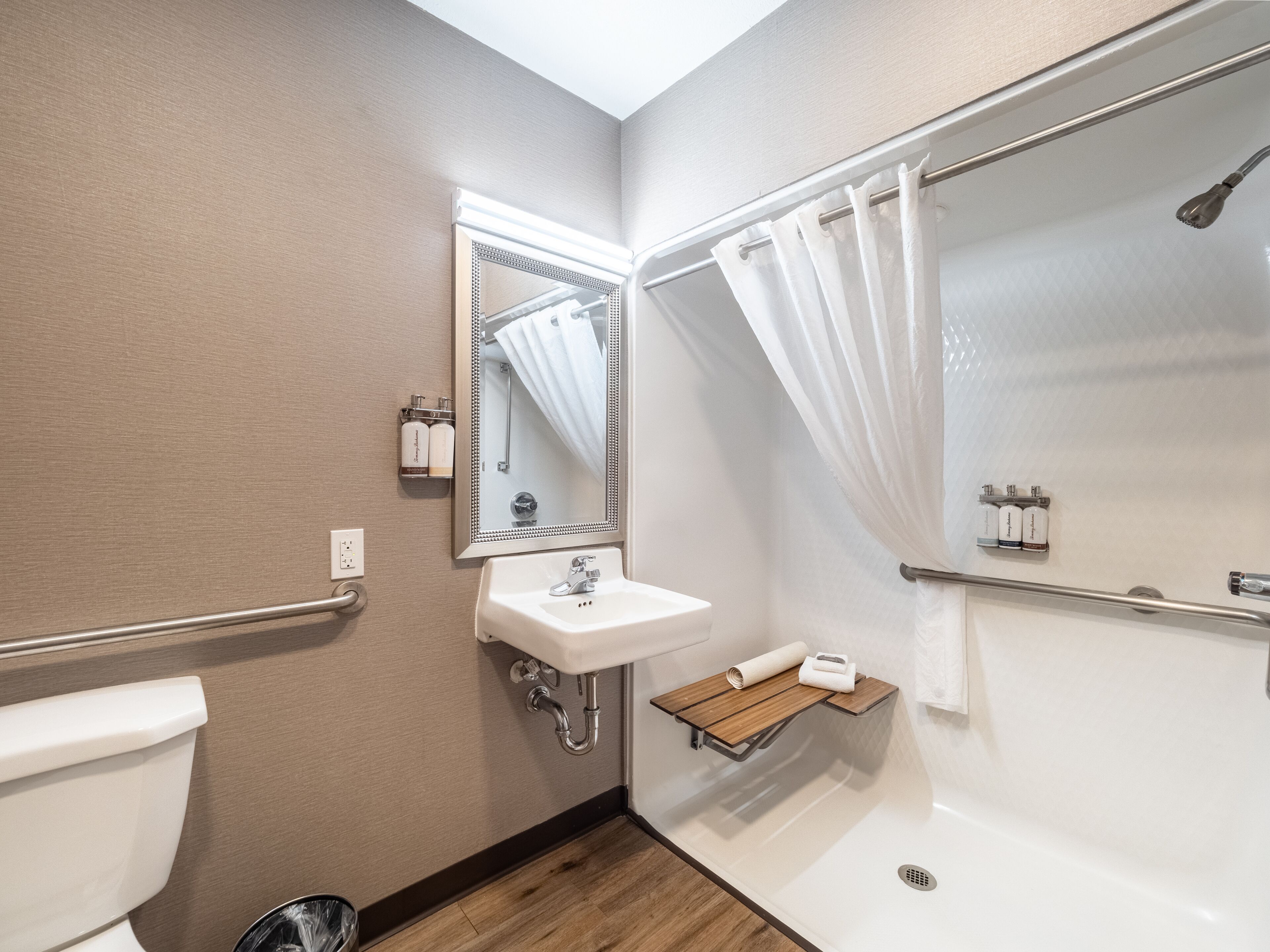 A bathroom with a toilet, sink, mirror, shower, and a shelf with toiletries.