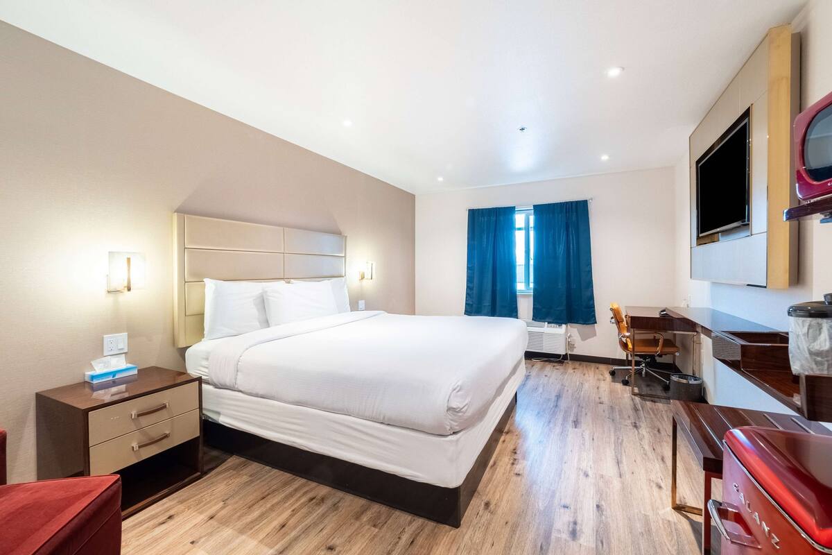 A hotel room with a bed, bedside table, desk, chair, and a TV mounted on the wall.