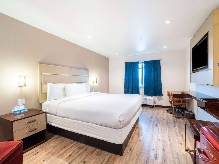 Habitación de hotel con cama, mesita de noche, escritorio, silla y televisor montado en la pared.