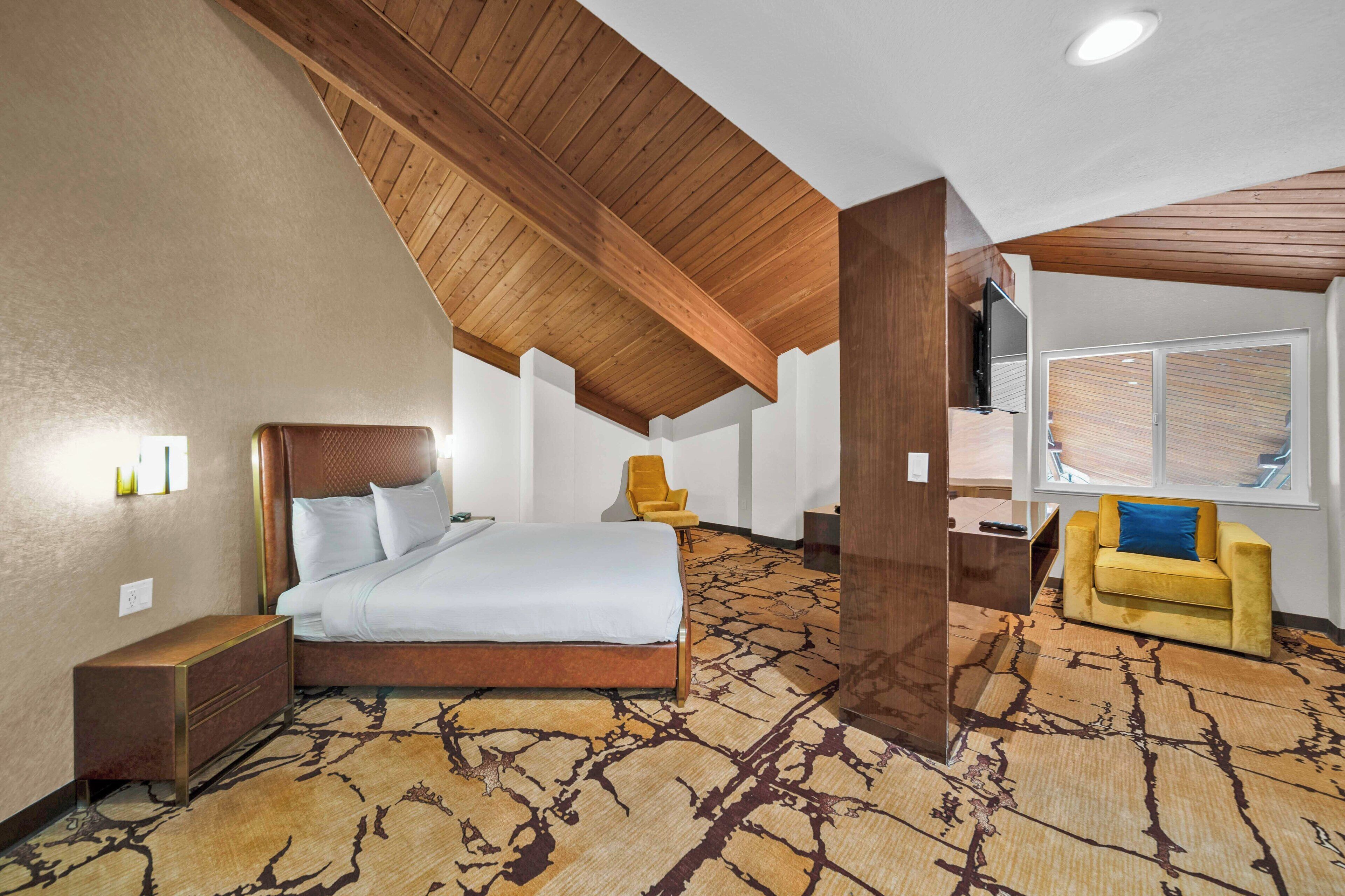 A hotel room with a large bed, a sofa, a TV, and a window with blinds.