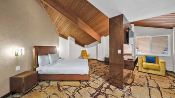 A hotel room with a large bed, a sofa, a TV, and a window with blinds.