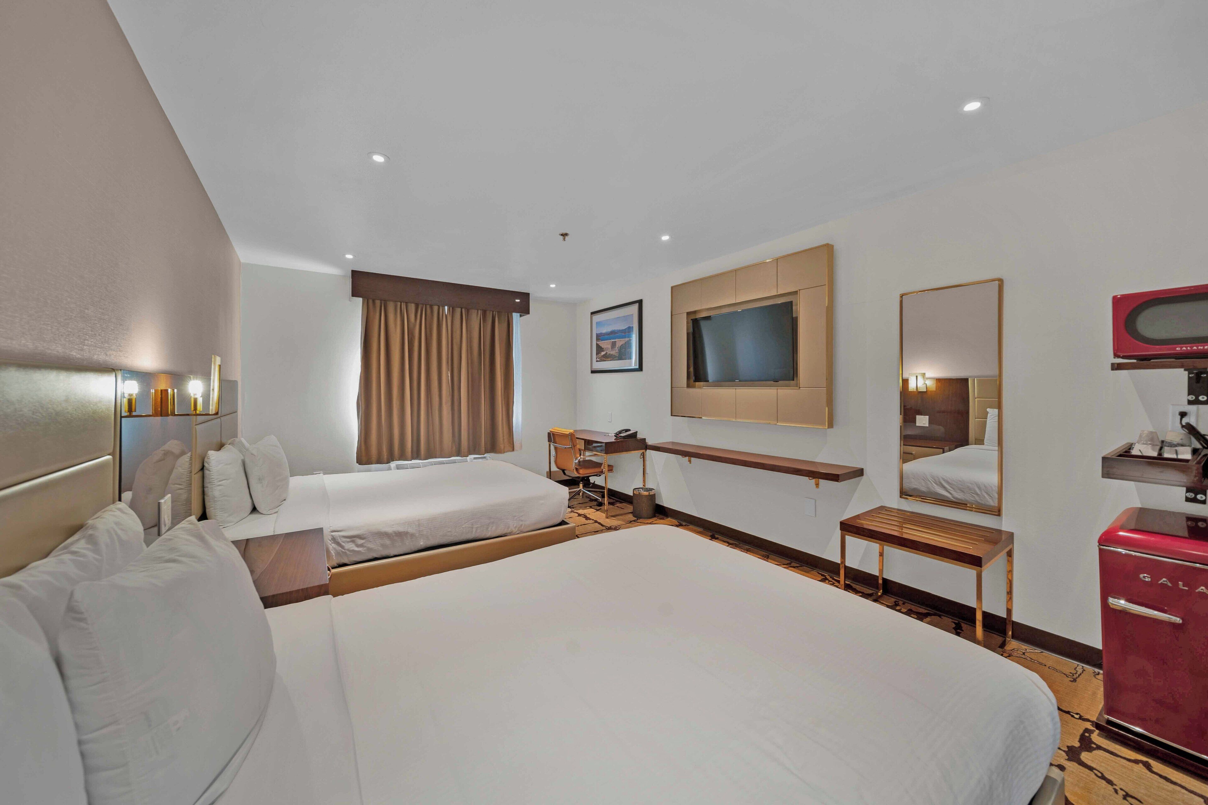 Habitación de hotel con dos camas, un escritorio, una silla, un televisor, un espejo y un minibar.