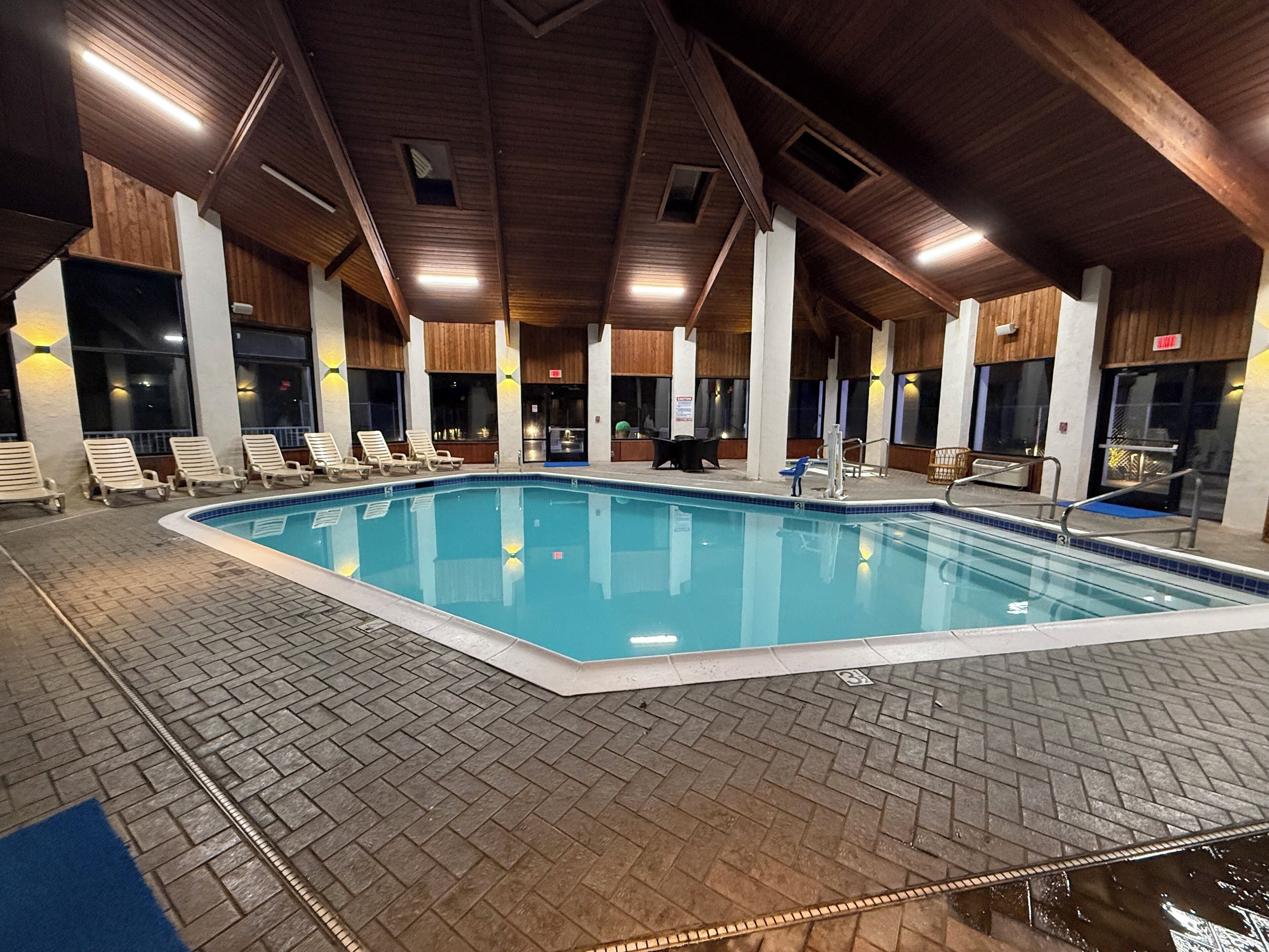 An indoor swimming pool with lounge chairs and a tiled floor.