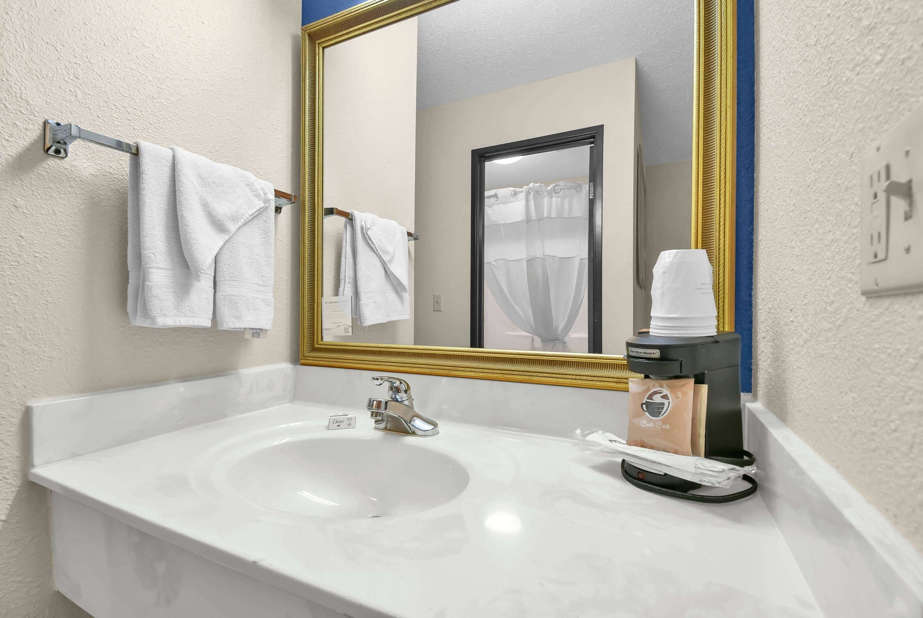 A bathroom with a white sink, a mirror with a gold frame, and a towel rack with two white towels.