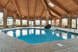 An indoor swimming pool with wooden beams, tiled flooring, and large windows. - Baymont by Wyndham Zanesville (Zanesville)