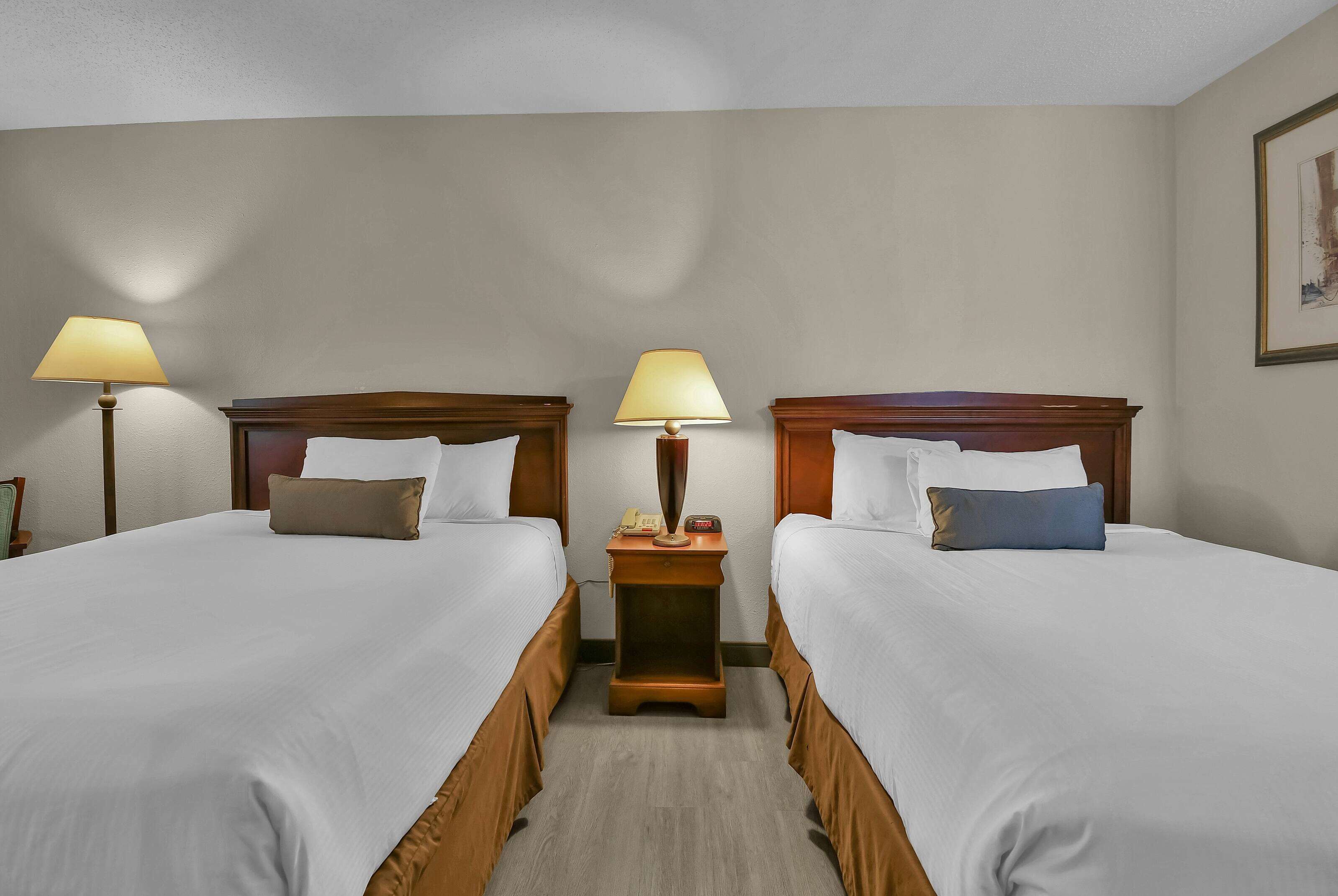 Habitación de hotel con dos camas, cada una con cabecera de madera, una mesita de noche con lámpara y un cuadro enmarcado en la pared.