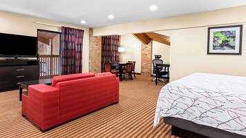 A hotel room with a large bed, a red sofa, a desk with a chair, a television, and a framed picture on the wall.