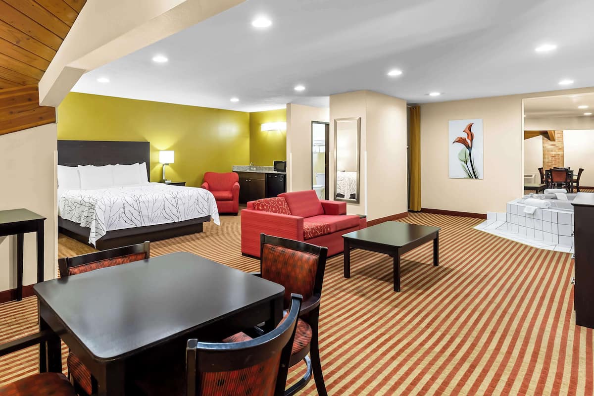 A hotel room with a bed, a red sofa, a dining table, and a small kitchenette.