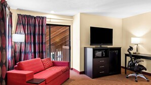 A hotel room with a red sofa, a flat-screen TV, a desk with a lamp, and a sliding door leading to a balcony. - Best Western Jacksonville Inn (Jacksonville)