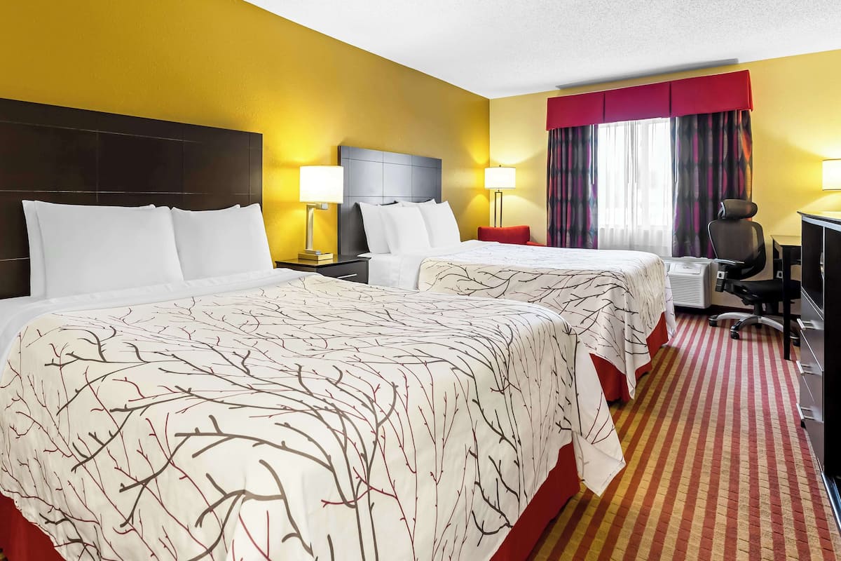 A hotel room with two beds, a desk, and a chair.