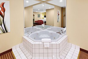 A bathroom with a large bathtub, a mirror, and a red chair in the background.