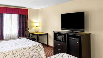 A hotel room with a bed, a desk with a lamp, a television, and a minibar.