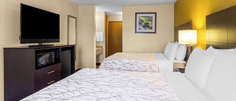Quarto de hotel com duas camas, televisão, escrivaninha e banheiro visível através de uma porta aberta.