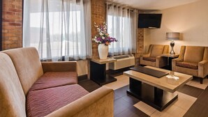 A modern living room with a sofa, two armchairs, a coffee table, a TV mounted on the wall, and a decorative vase with flowers. - Best Western Jacksonville Inn (Jacksonville)