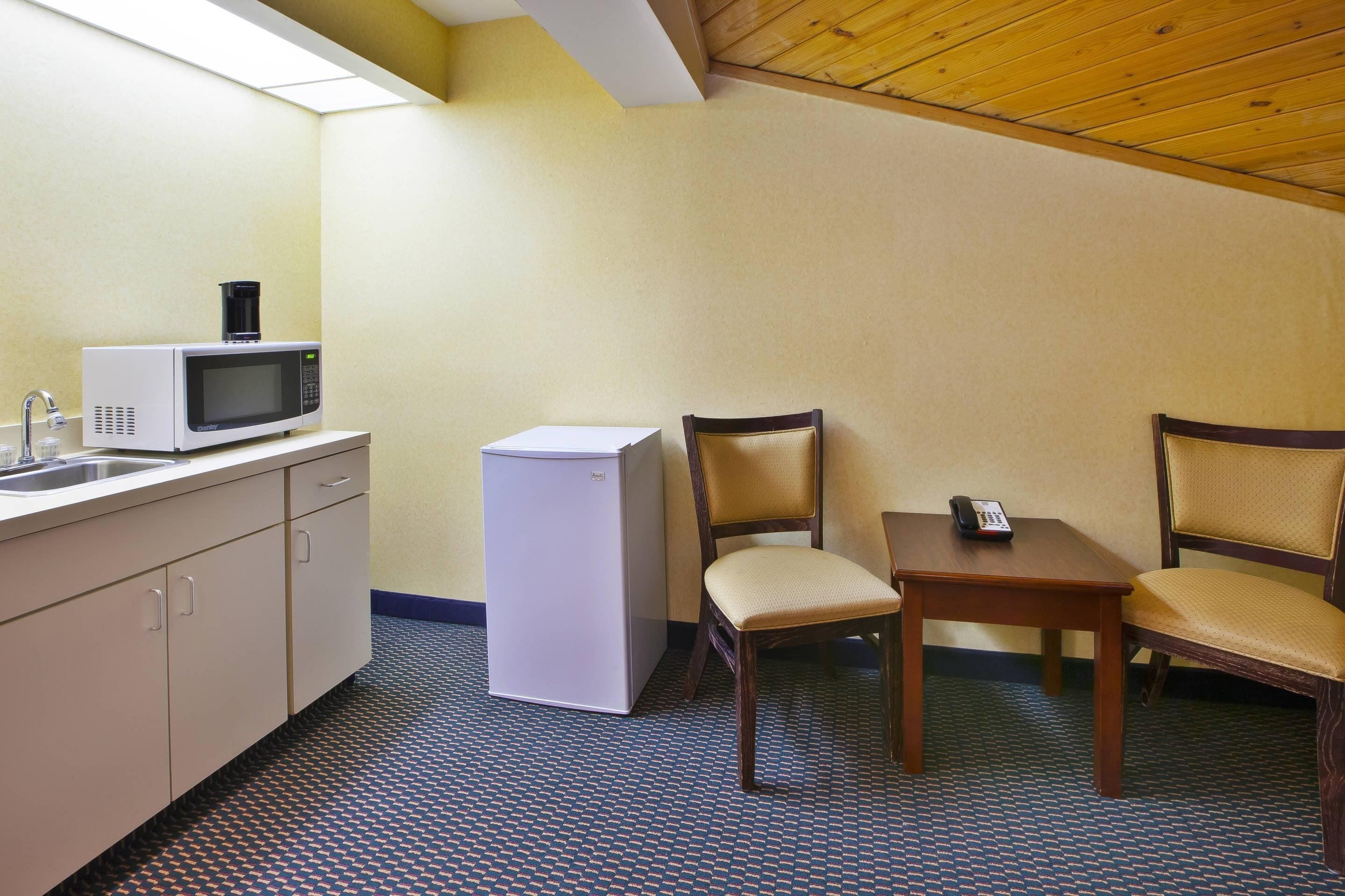A small kitchenette with a microwave, refrigerator, sink, and a table with two chairs.