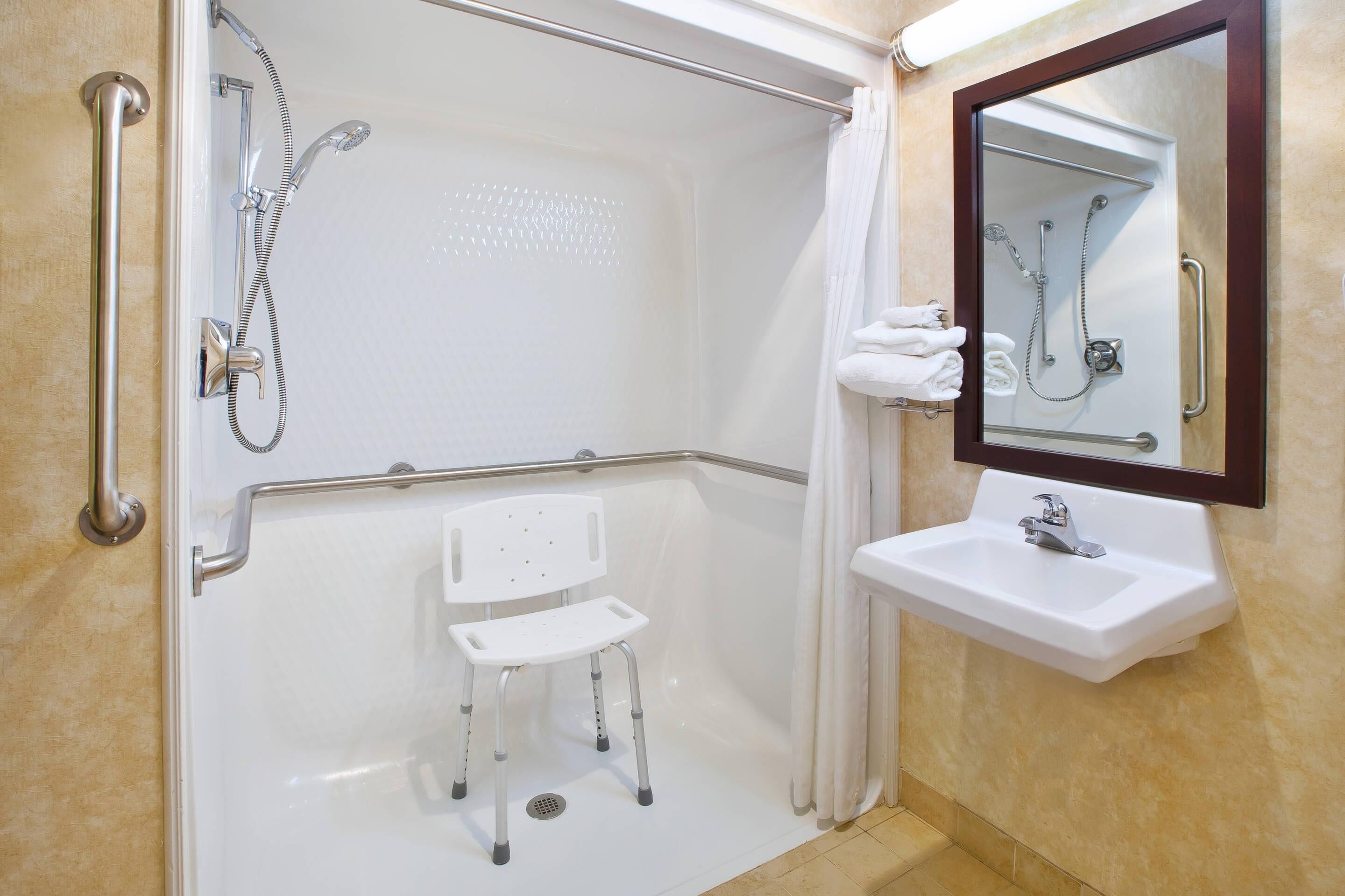 Un baño con ducha, lavamanos, una silla y un espejo.