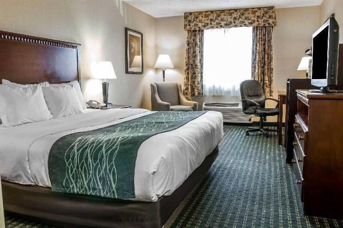 Una habitación de hotel con una cama grande, dos sillas, un escritorio con una computadora y un televisor.