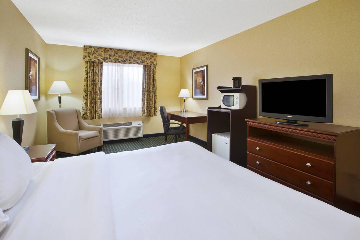 Una habitación de hotel con cama, escritorio, silla, televisión, microondas y cómoda.