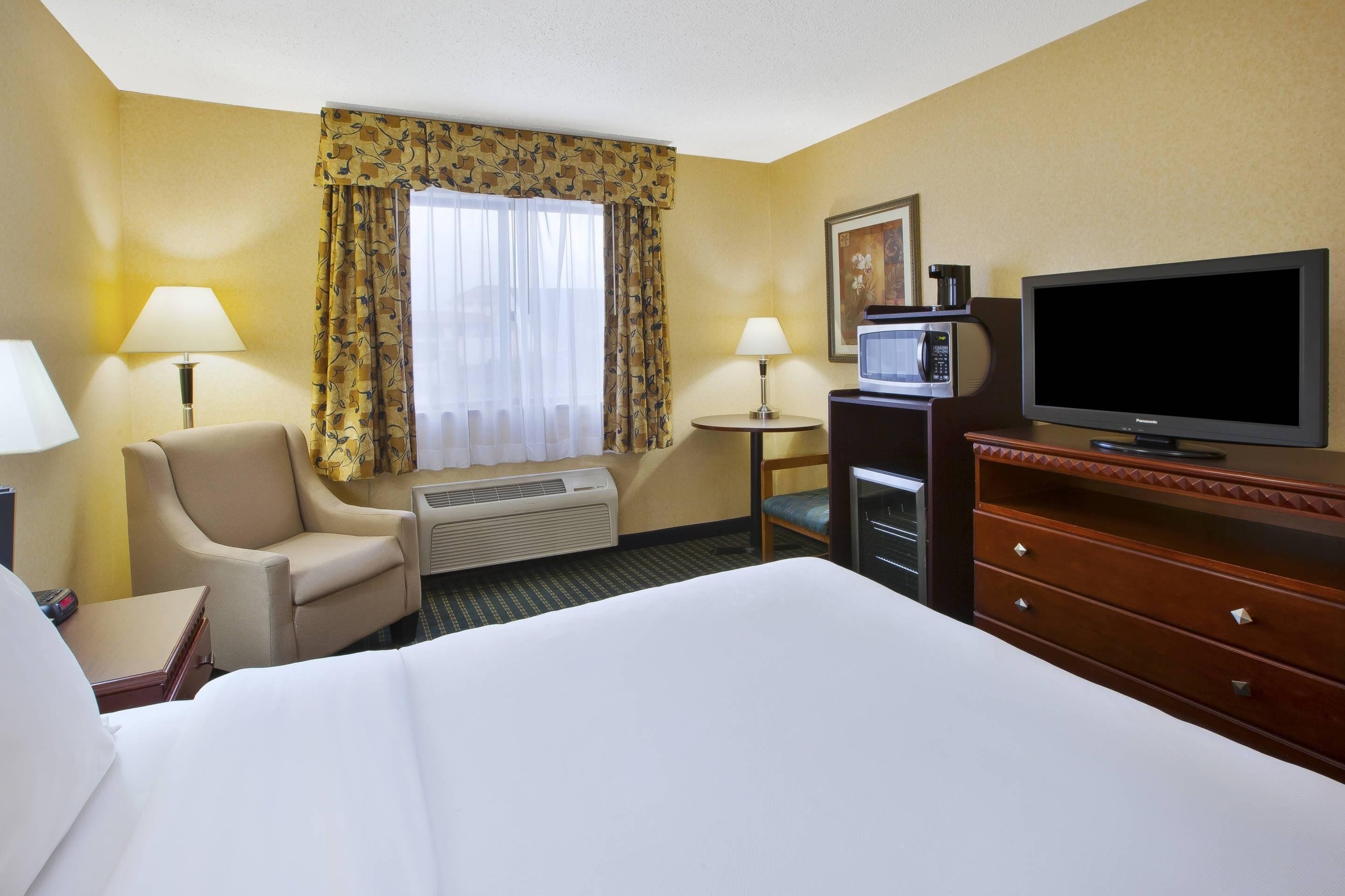 Una habitación de hotel con cama, una silla, escritorio, televisor y aire acondicionado.