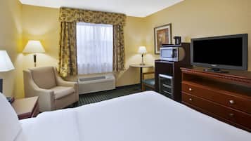 Una habitación de hotel con cama, una silla, escritorio, televisor y aire acondicionado.