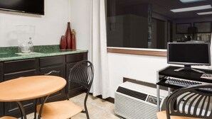 Una cocina con una mesa de comedor, sillas, un televisor montado en la pared y una computadora.