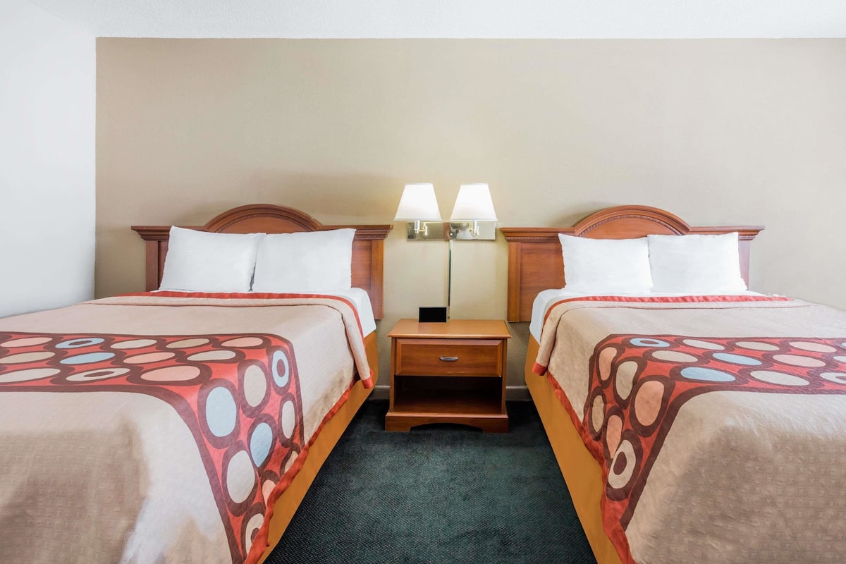 Una habitación de hotel con dos camas, cada una con una colcha estampada, una mesita de noche con lámpara y un pequeño cajón.