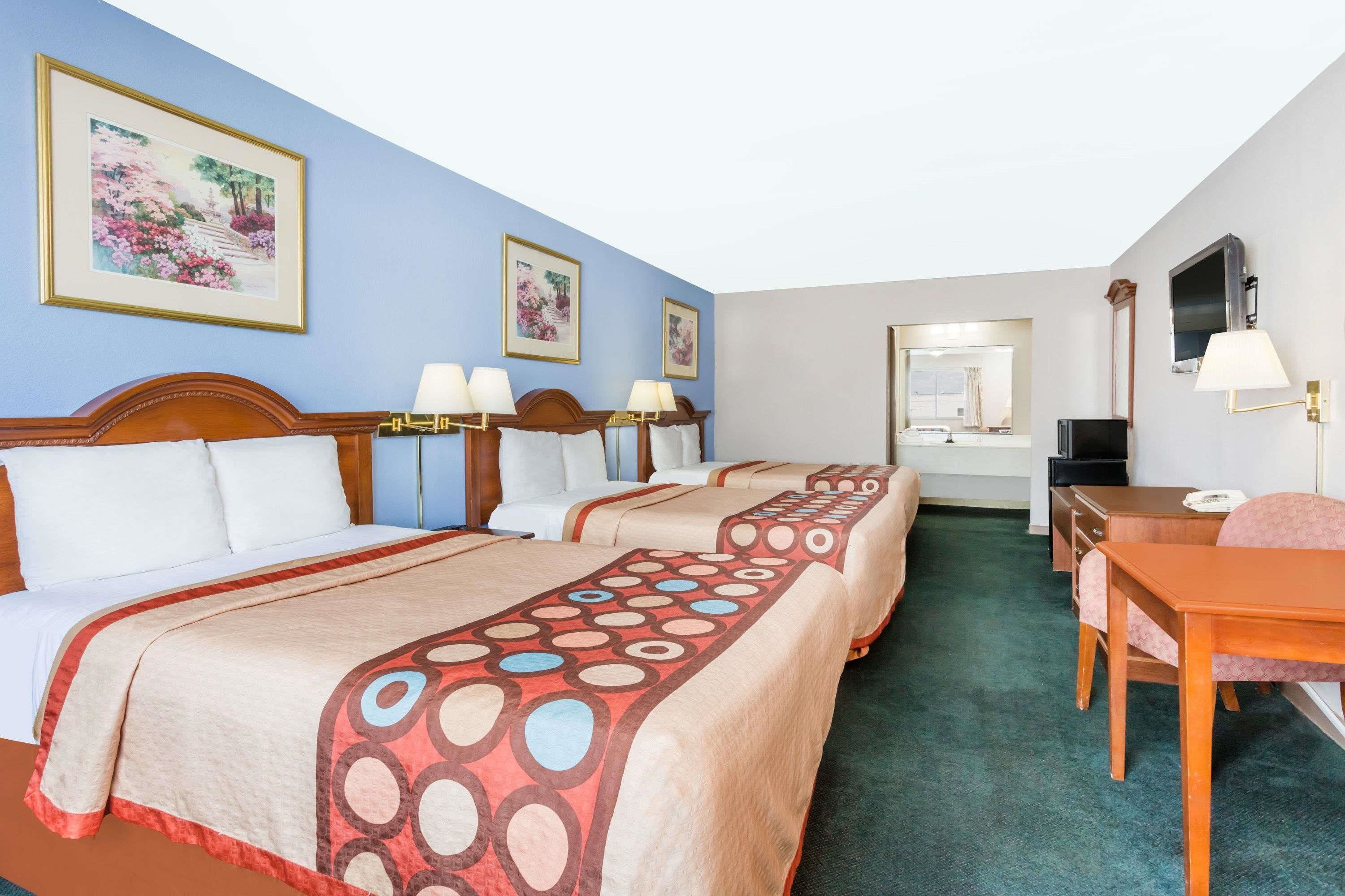 A hotel room with two beds, a desk, a chair, a TV, and framed pictures on the wall.