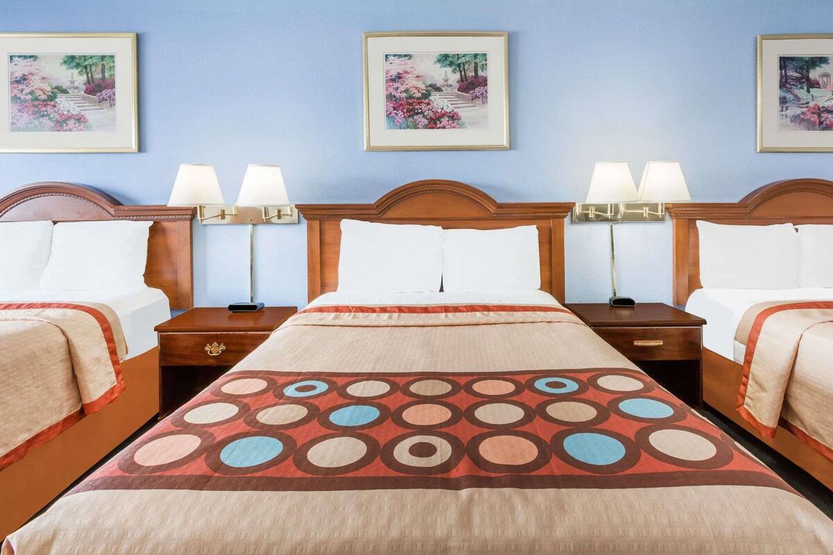 Habitación de hotel con tres camas, cada una con cabecero de madera, ropa de cama blanca y una colcha estampada. Hay tres cuadros enmarcados en la pared sobre las camas.
