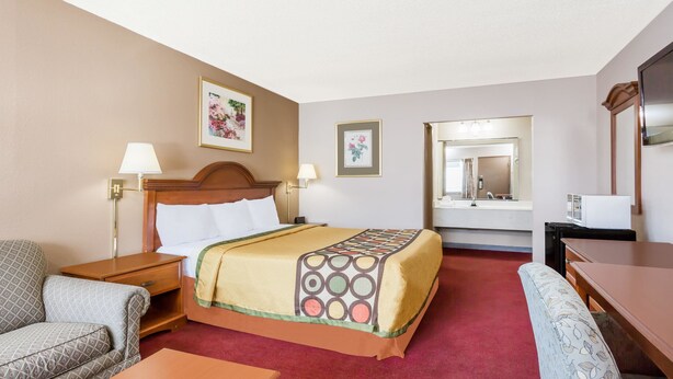 Habitación de hotel con cama, escritorio, silla, sofá, mesita de noche, lámpara y espejo.