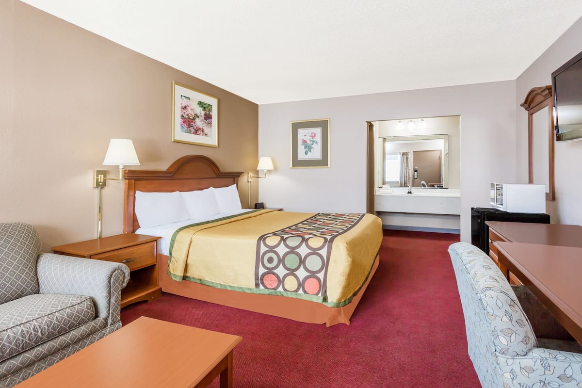 Habitación de hotel con cama, escritorio, silla, sofá, mesita de noche, lámpara y espejo.