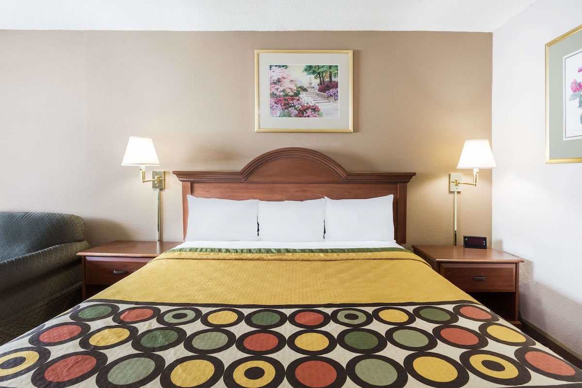 Una habitación de hotel con una cama, dos mesitas de noche, un sofá verde y dos lámparas de pared.