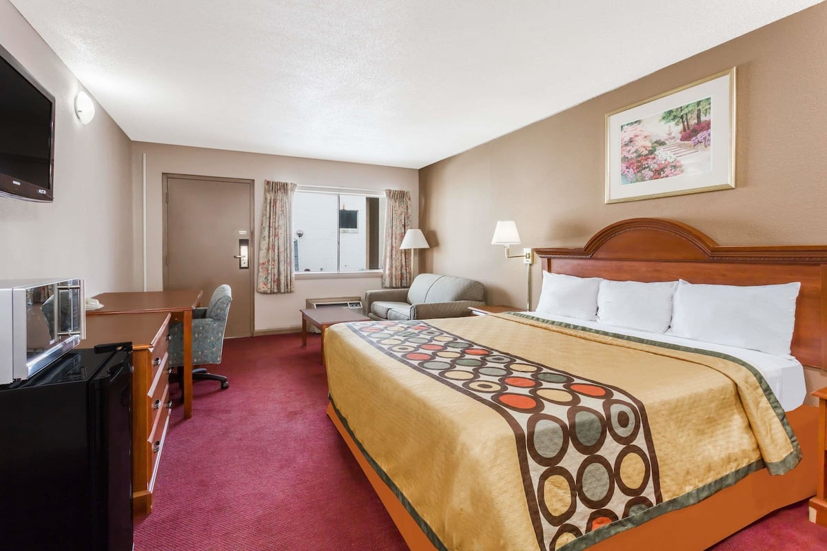 Una habitación de hotel con cama, escritorio, silla, televisión y un cuadro en la pared.