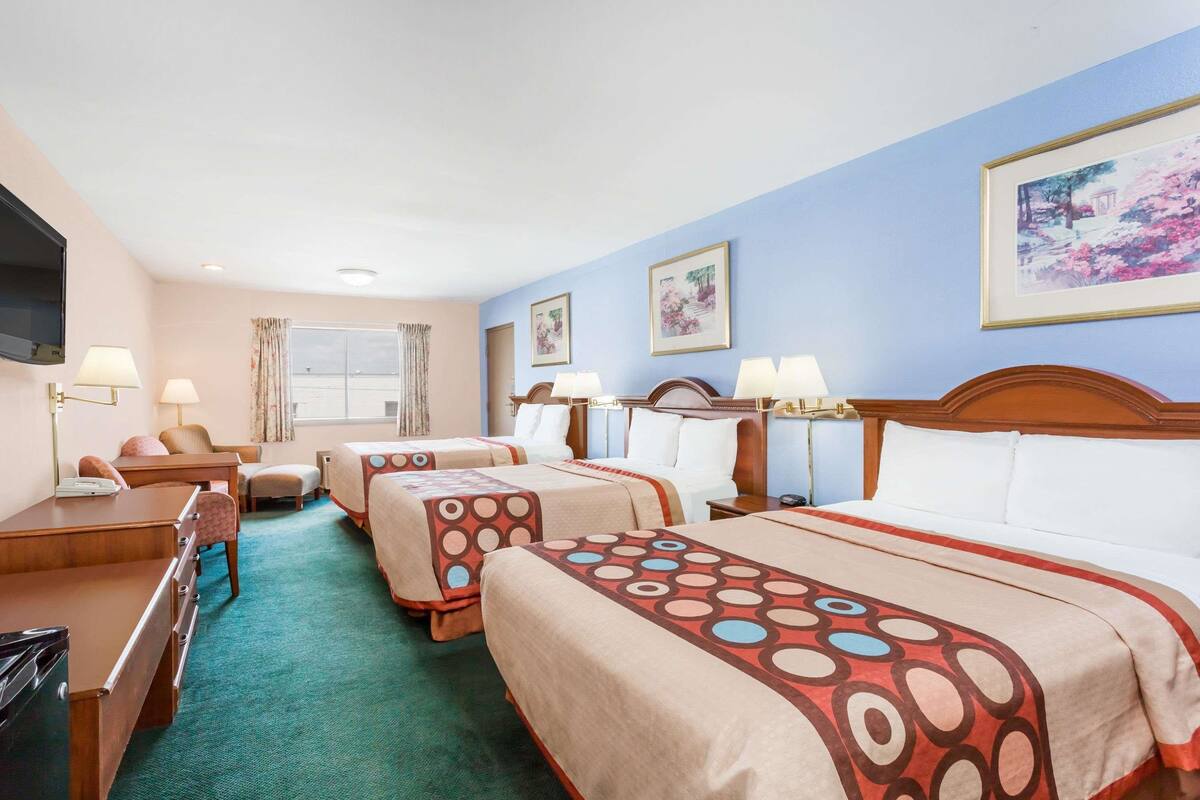 Habitación de hotel con dos camas, un escritorio, una silla, un televisor y un ventanal con cortinas.