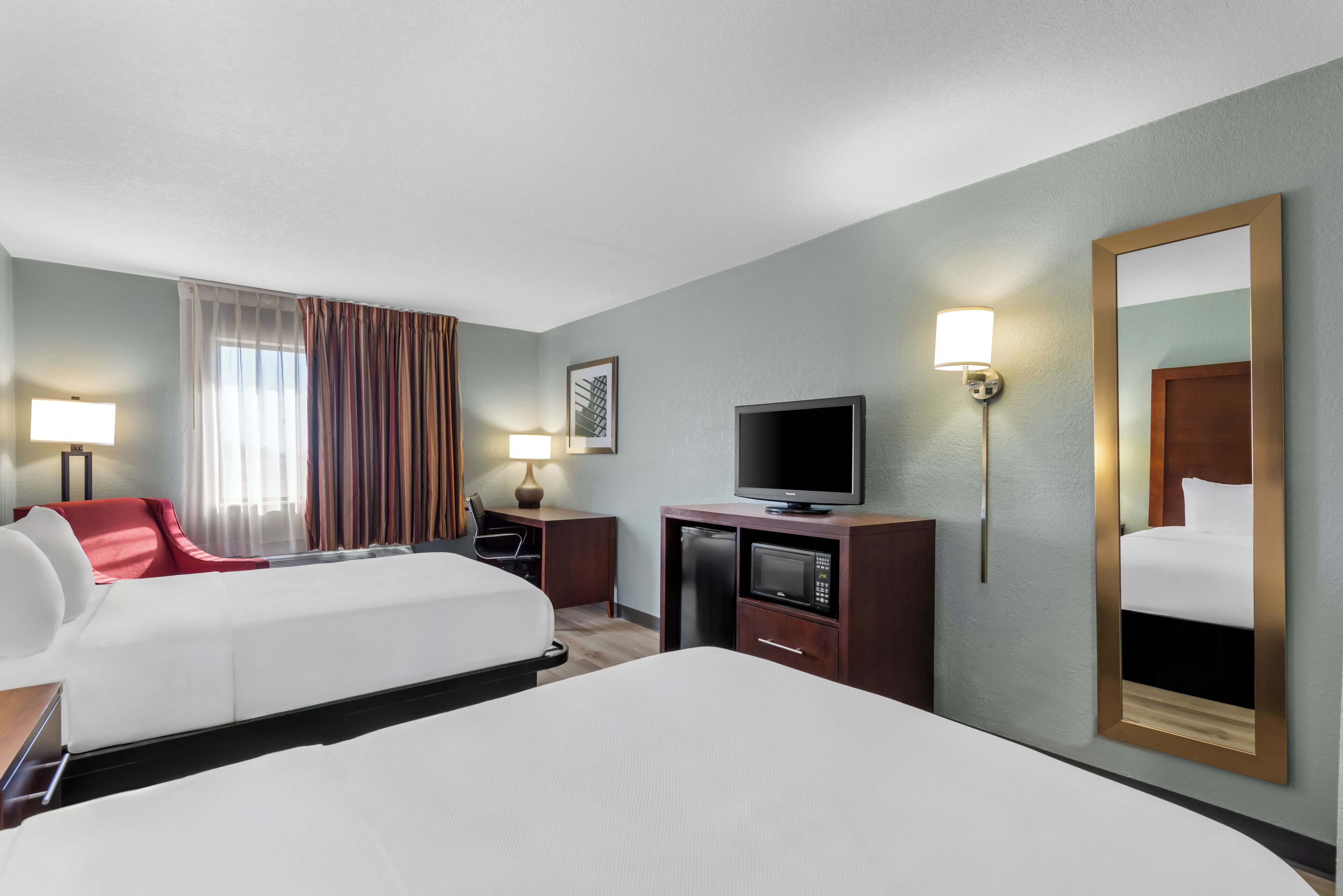 A hotel room with a bed, a desk with a television, a chair, a lamp, and a mirror.