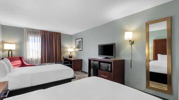 A hotel room with a bed, a desk with a television, a chair, a lamp, and a mirror.
