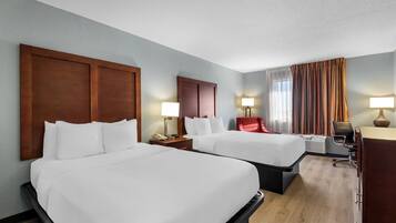 A hotel room with two beds, a desk, a chair, a lamp, and a window with curtains.
