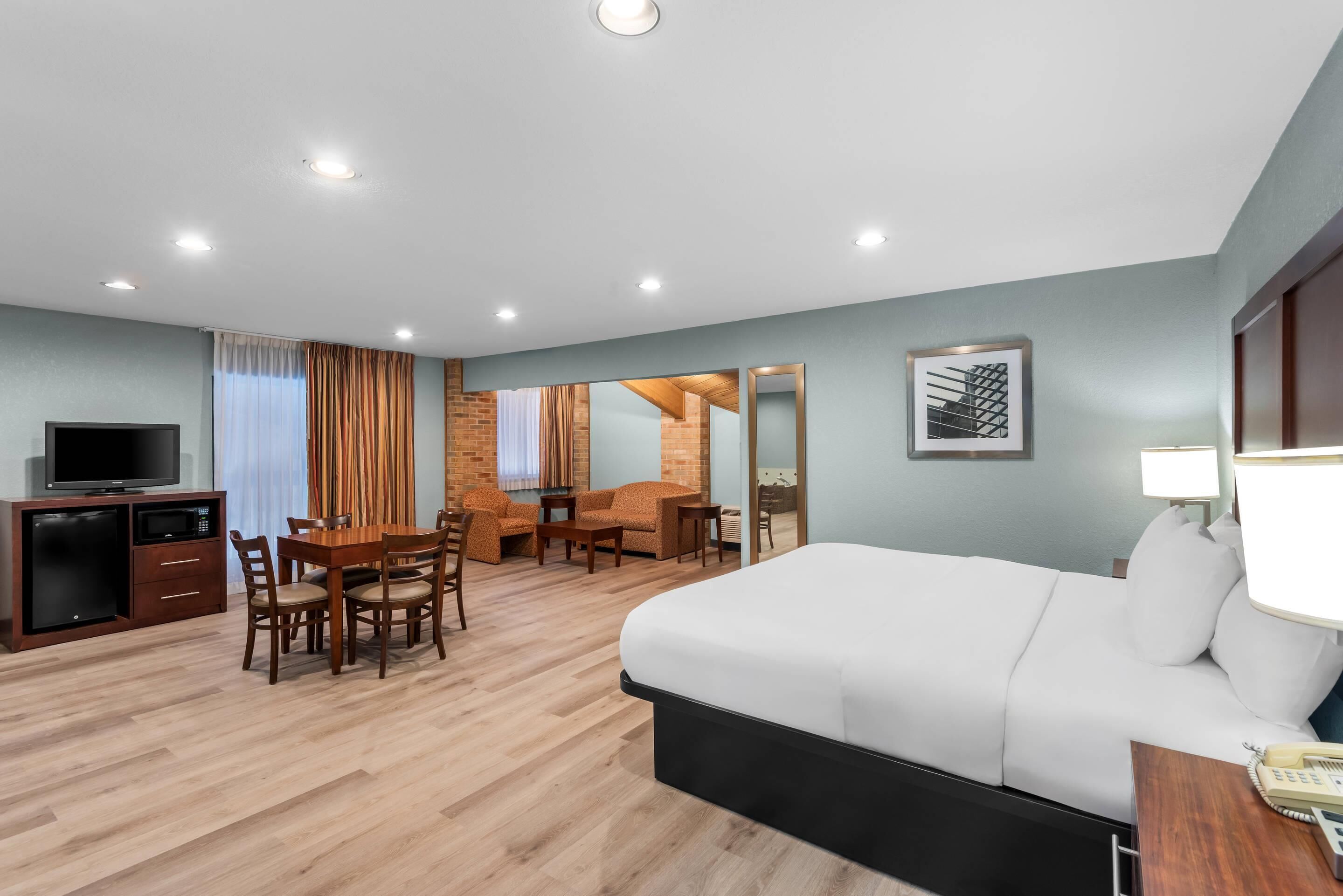 A hotel room with a bed, a desk, a TV, and a dining area.
