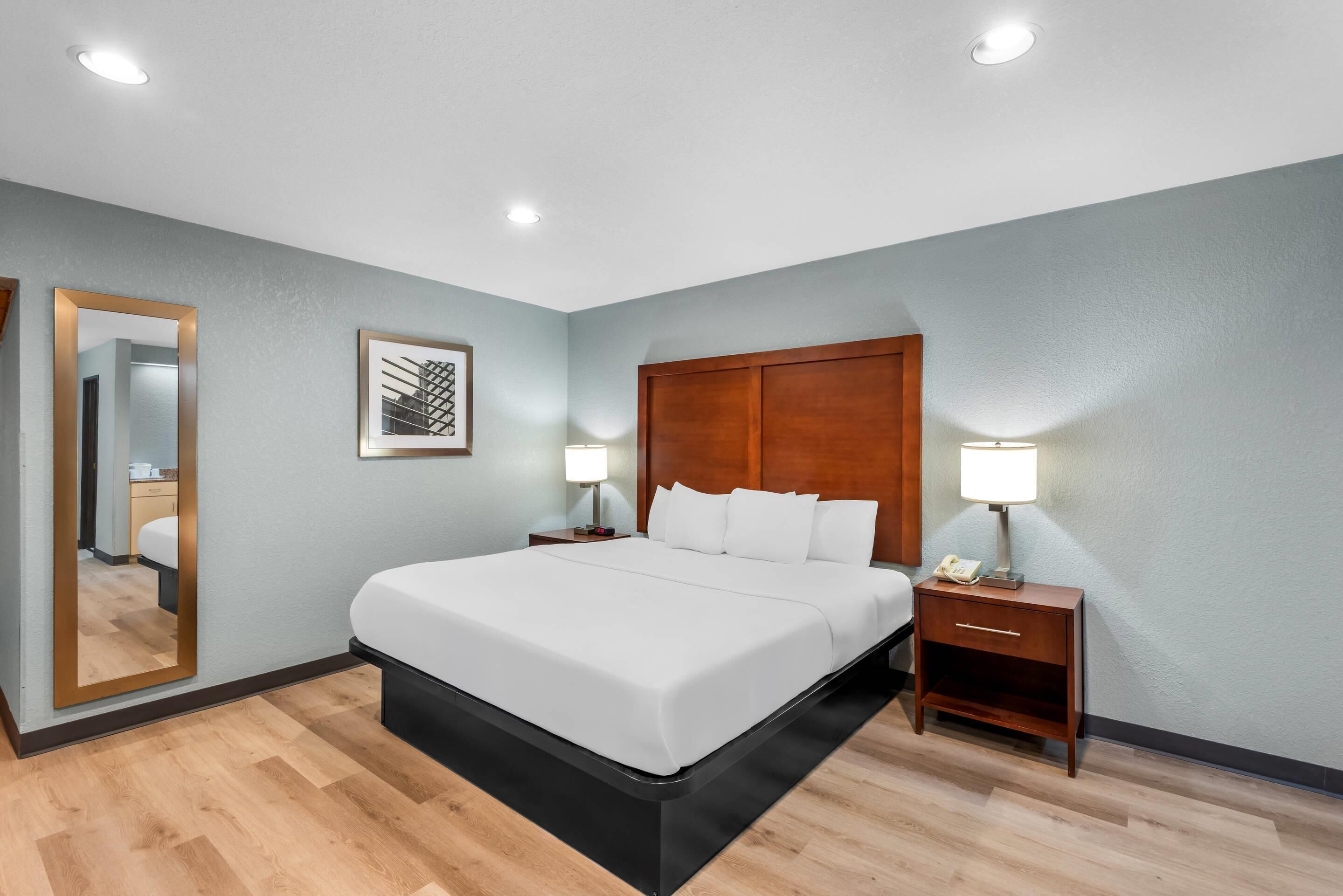 A hotel room with a bed, bedside tables, a mirror, and a wall-mounted picture.