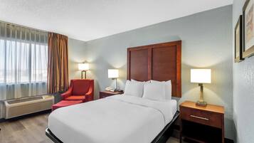 A hotel room with a large bed, a red chair, two bedside tables with lamps, a wooden headboard, and a window with curtains.
