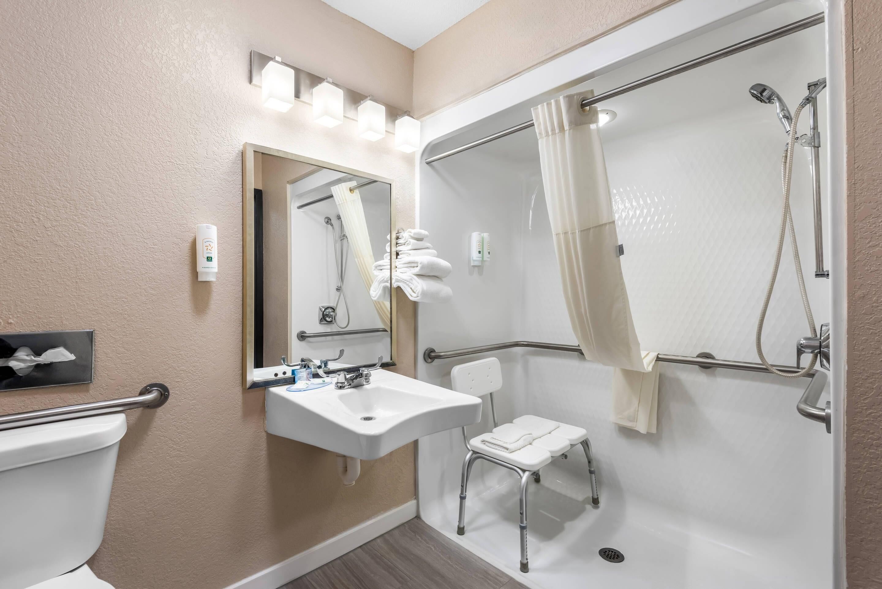 A bathroom with a toilet, sink, mirror, shower, and a small step stool.