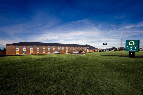 A Quality Inn by Choice Hotel with a brick facade, multiple windows, and a parking lot.