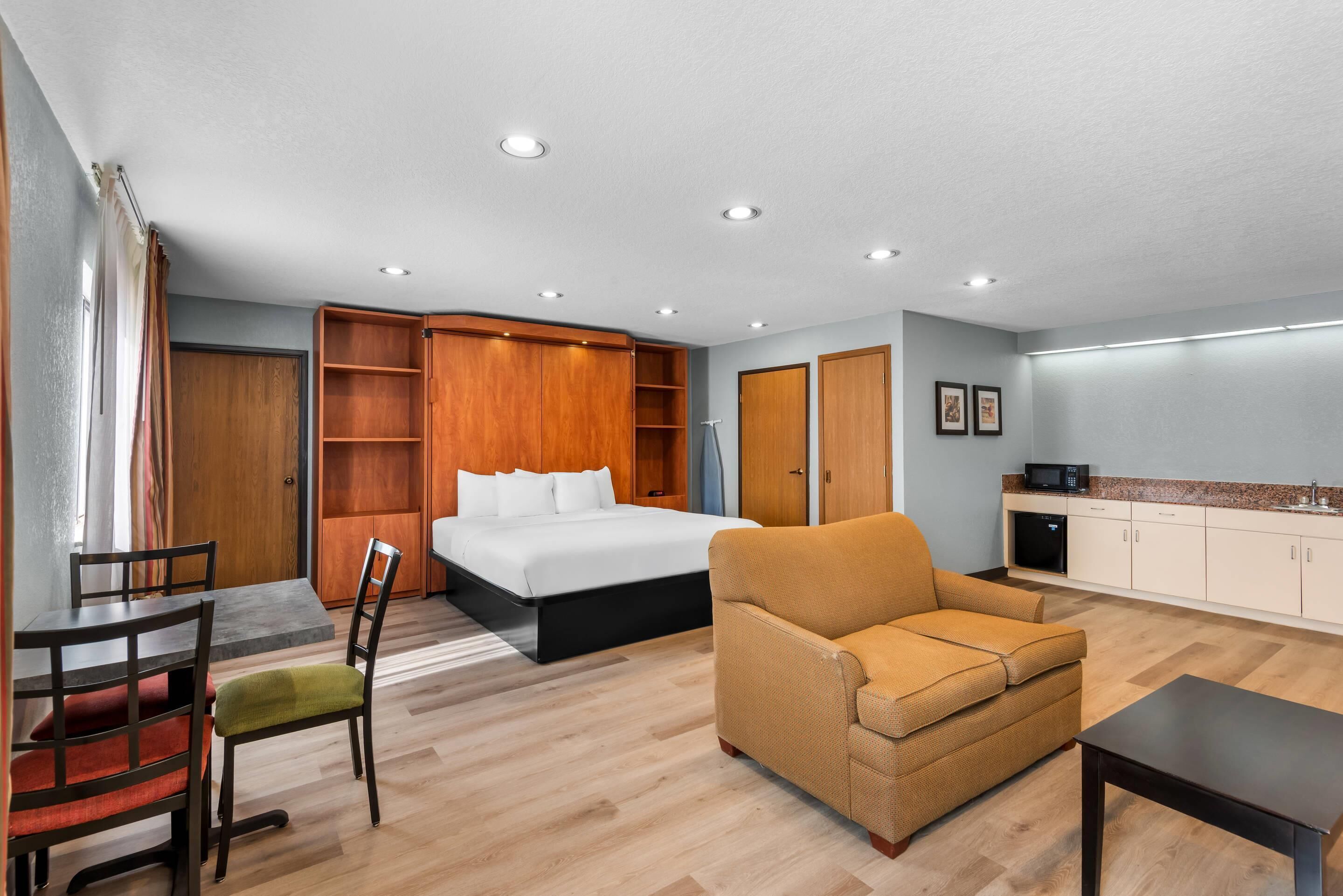 A hotel room with a bed, a sofa, a dining table, and a kitchenette.