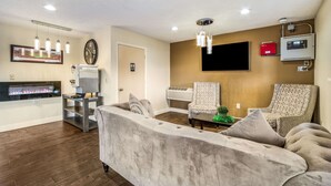 A living room with a fireplace, two armchairs, a sofa, a flat-screen TV, and a ceiling-mounted air conditioning unit. - Quality Inn Columbia Airport (West Columbia)