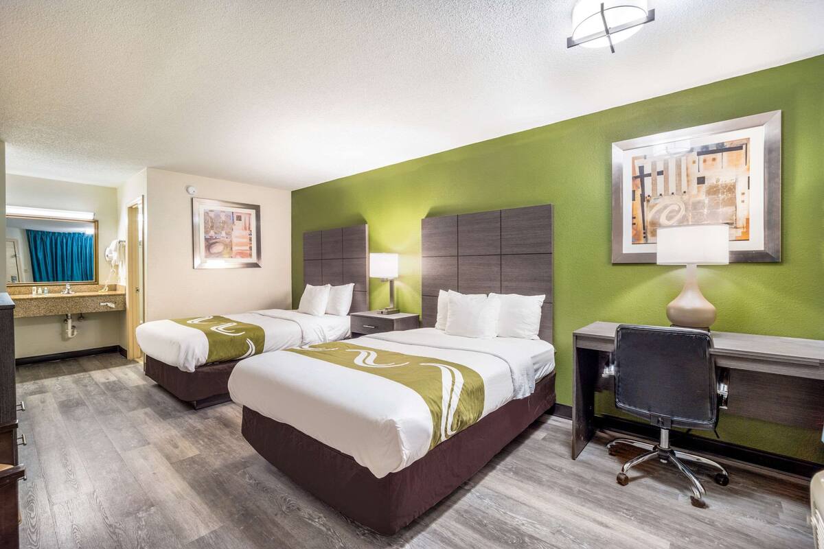 A hotel room with two beds, a desk, and a chair.