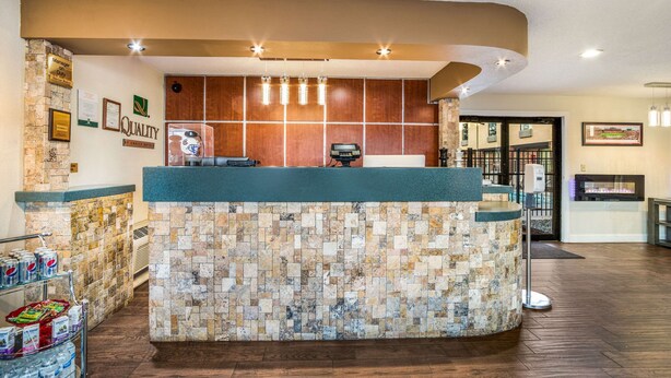 A reception area with a stone mosaic wall, a wooden reception desk, and a counter with a green top. There are framed certificates on the wall and a vending machine to the right. - Quality Inn Columbia Airport (West Columbia)