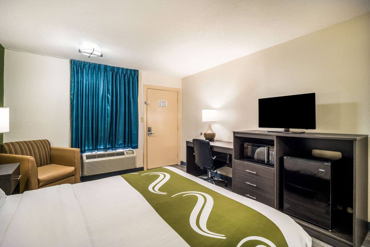 A hotel room with a bed, a desk, a television, a minibar, and a window with curtains.